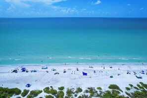 A beach with clear turquoise water, white sand, and sparse vegetation.