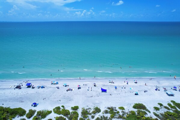 A beach with clear turquoise water, white sand, and sparse vegetation.