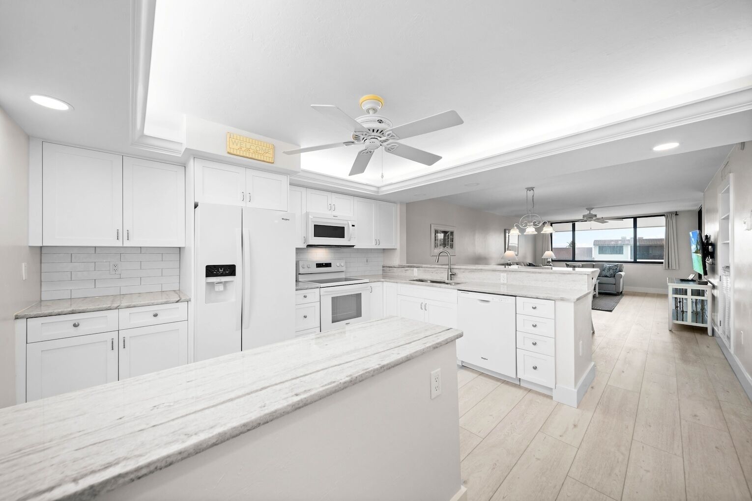 Une cuisine moderne avec des meubles blancs, un îlot central et un ventilateur de plafond.