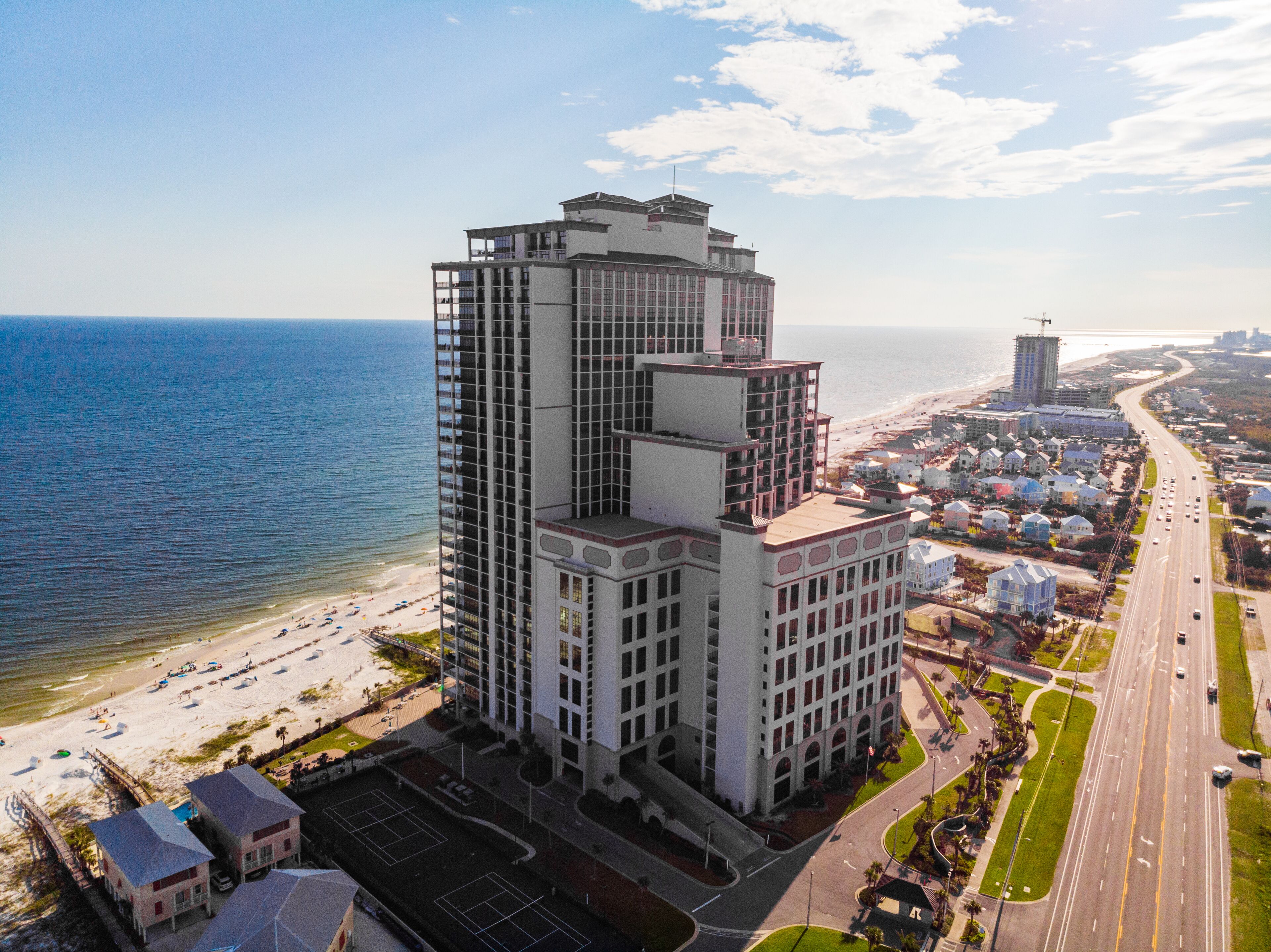 A high-rise hotel with multiple floors, a beach view, and a parking area.