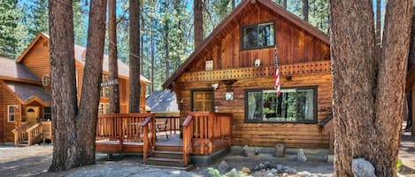 A wooden cabin with a porch, surrounded by tall trees.