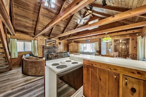 A rustic cabin interior with a kitchen area featuring a stove, wooden cabinets, and a dining table.