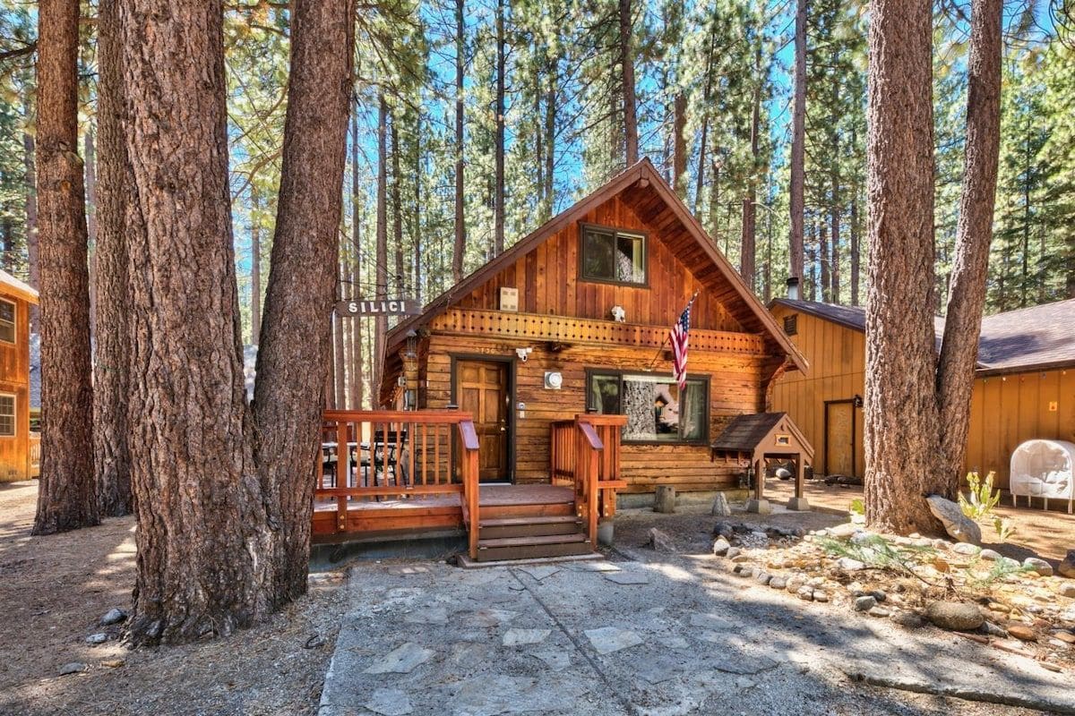 A wooden cabin with a porch, surrounded by tall trees.