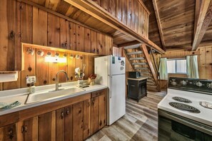 Cocina de cabaña de madera con una isla central, un refrigerador, una estufa y un microondas.