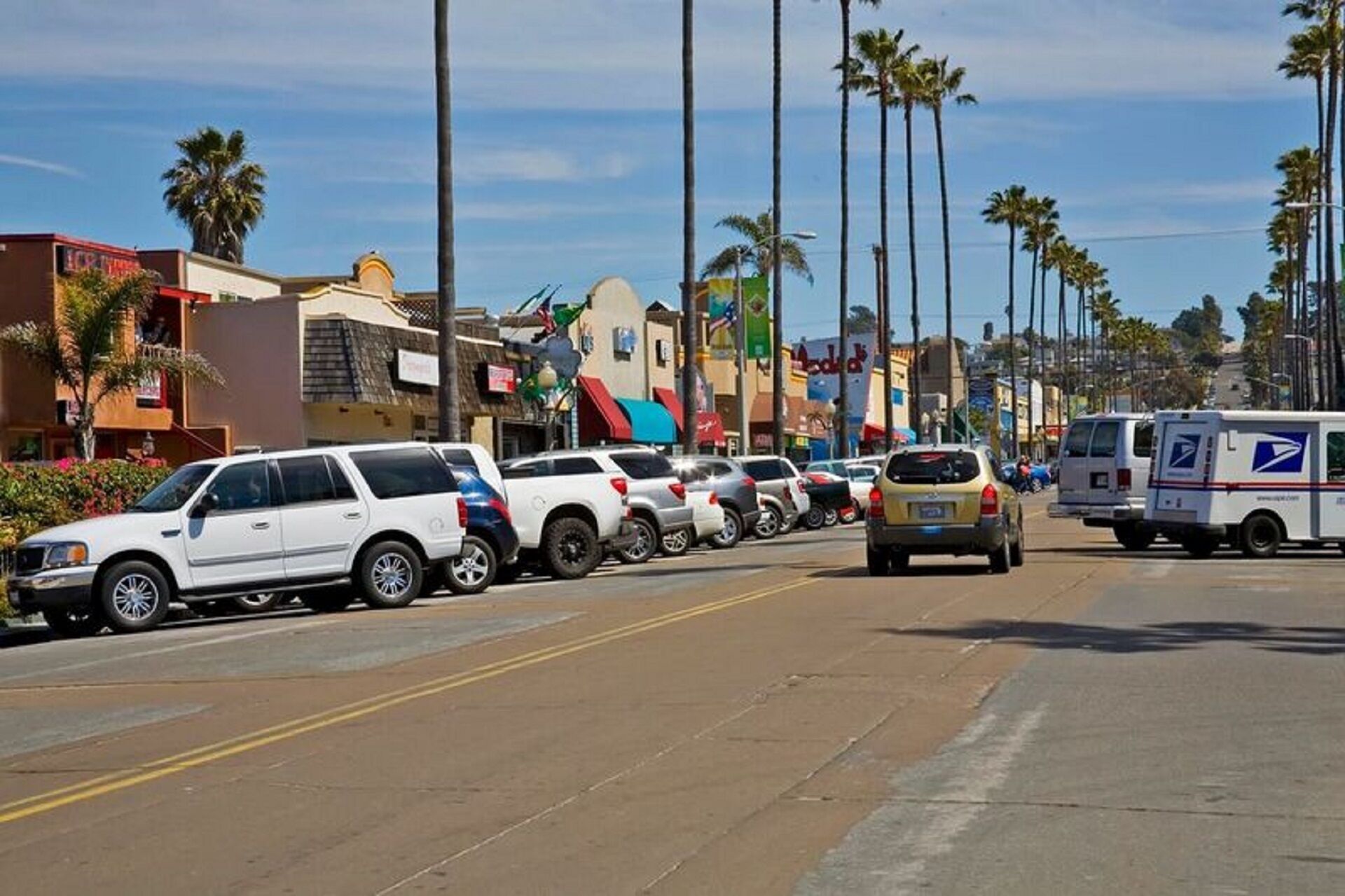A street lined with parked cars and a USPS mail truck.