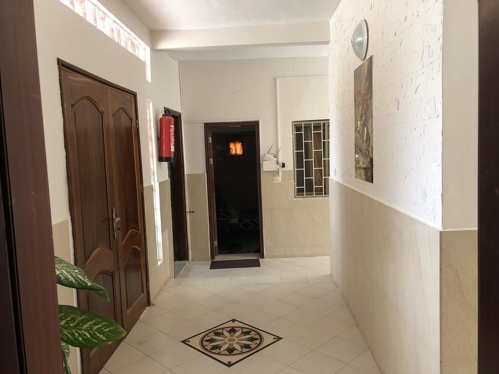A hallway with a tiled floor, a wooden door, a fire extinguisher, and a door with a window.