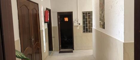 A hallway with a tiled floor, a wooden door, a fire extinguisher, and a door with a window.