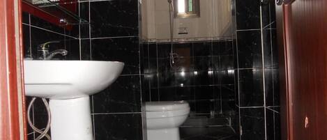 A bathroom with a white sink, a toilet, and black tiled walls.