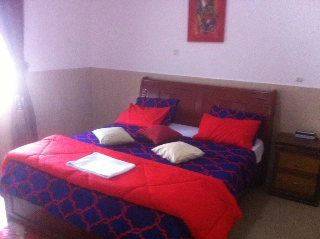A bed with a red and blue patterned bedspread, two pillows, and a white towel.