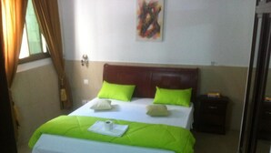 A bed with green and white bedding, a wooden headboard, and a small bedside table with a lamp. - Residence La Suite (St. Louis)