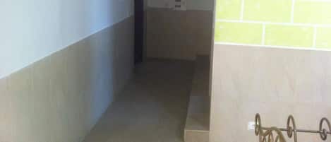 Un pasillo estrecho con una pared de azulejos a la derecha y una puerta al final.