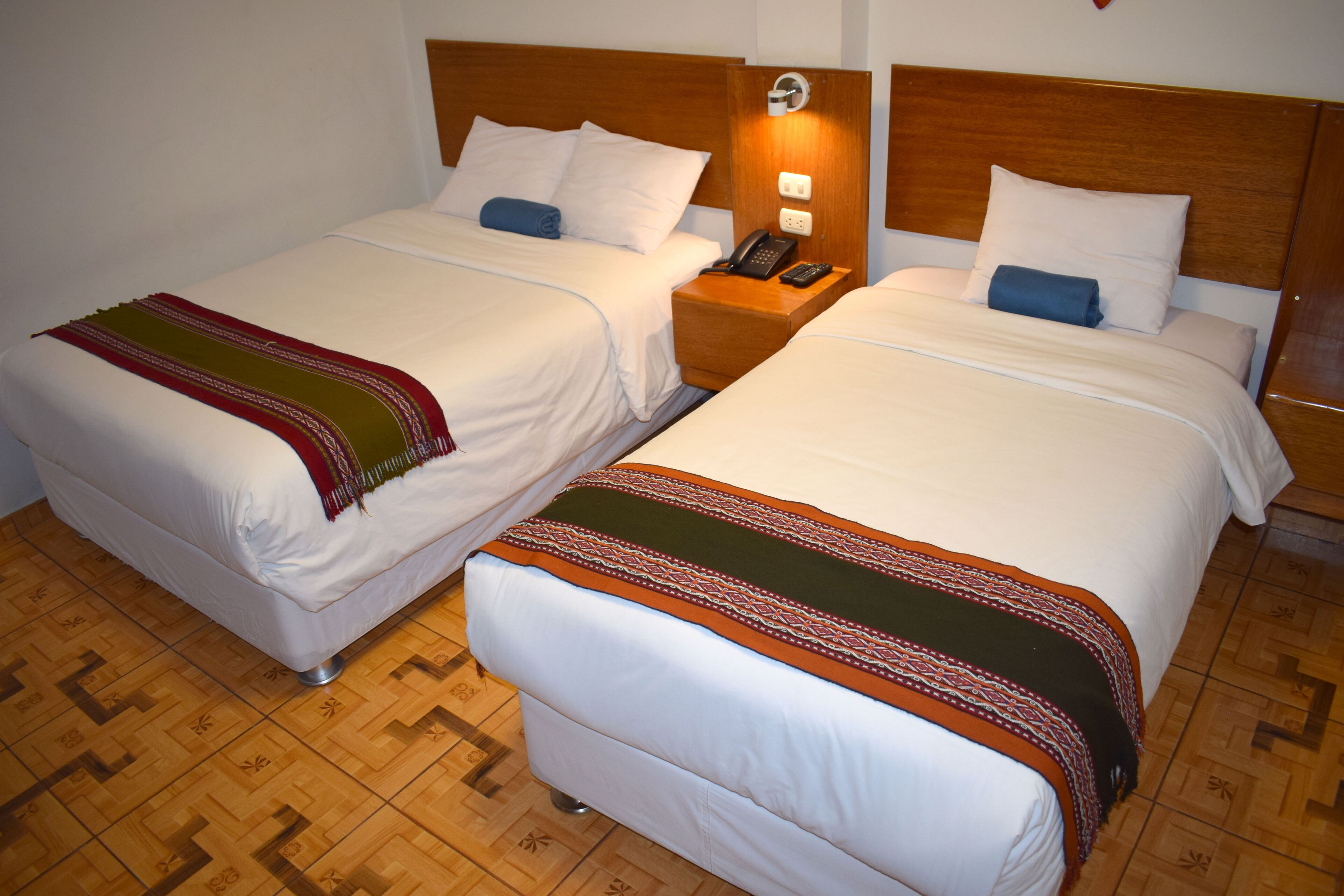 Two single beds with wooden headboards, a bedside table with a phone and lamp, and a patterned floor.