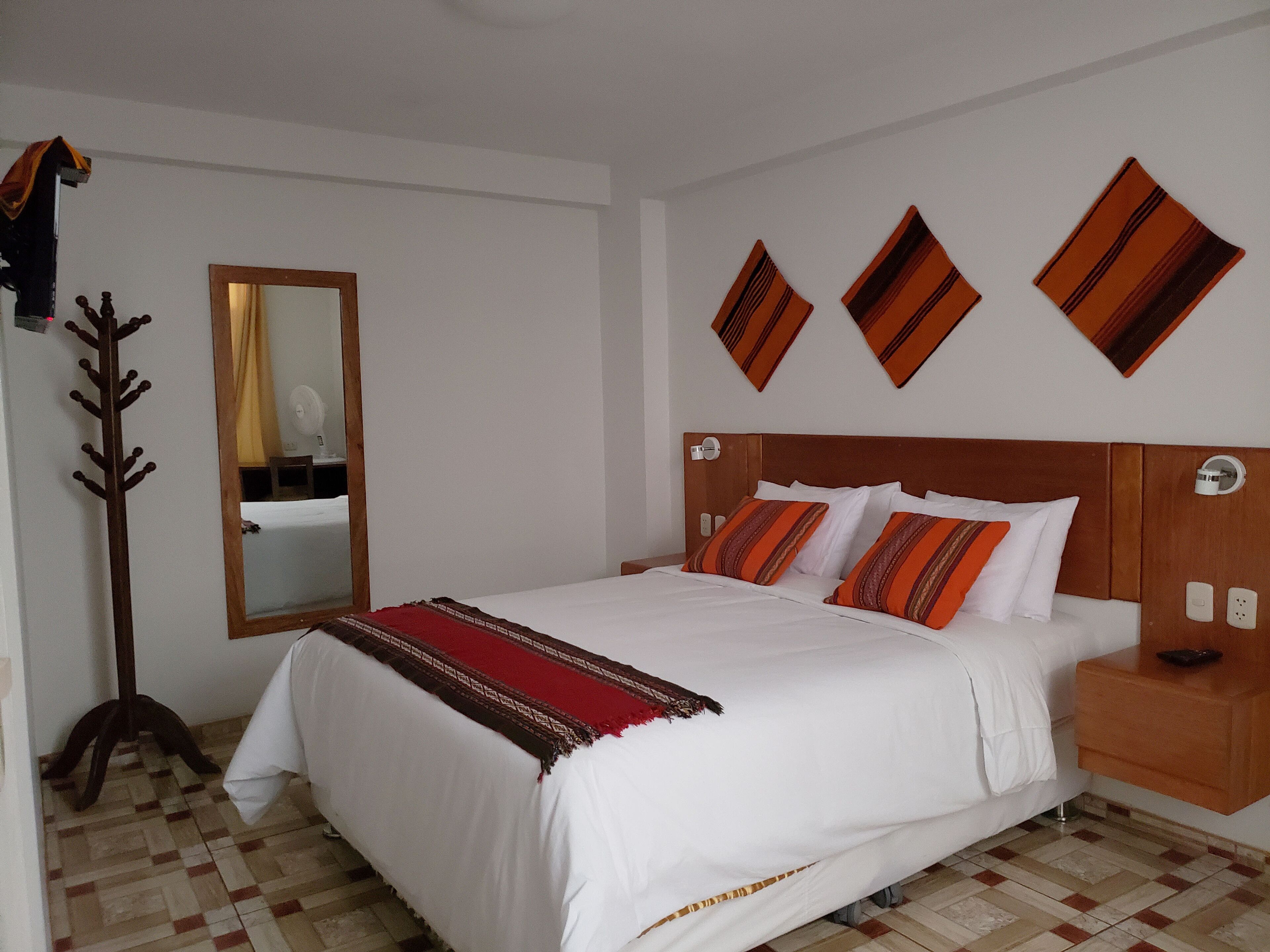 Ein Hotelzimmer mit einem großen Bett, einem Holz-Kopfstück, einem Nachttisch, einem Spiegel und einer Wandleuchte.