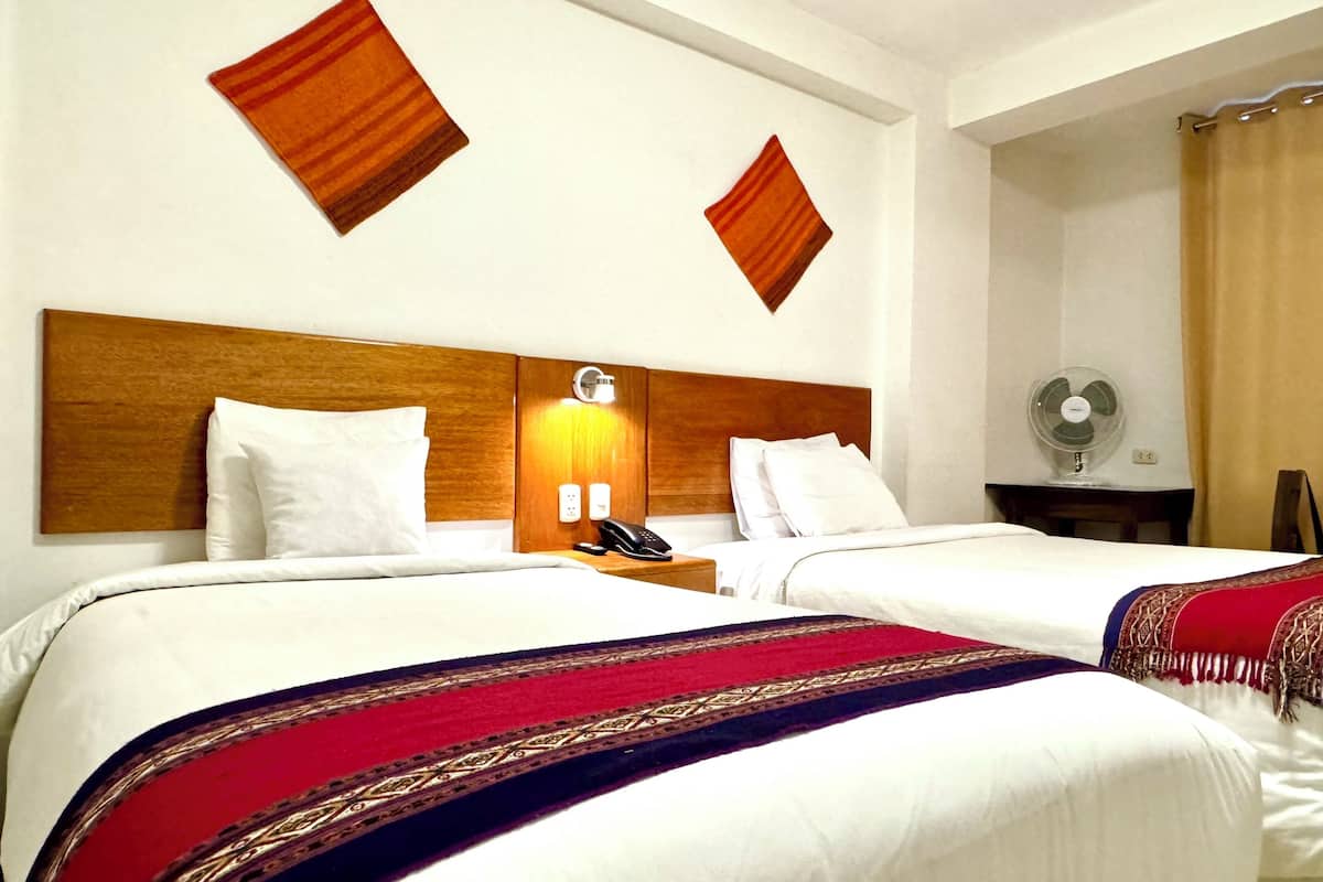 A hotel room with two beds, a wooden headboard, bedside lamps, a telephone, and a fan.
