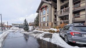 A multi-story building with a stone facade, balconies, and a parking area with a snow-covered ground.