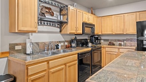 A kitchen with wooden cabinets, granite countertops, a stainless steel sink, a black stove, and a black refrigerator.