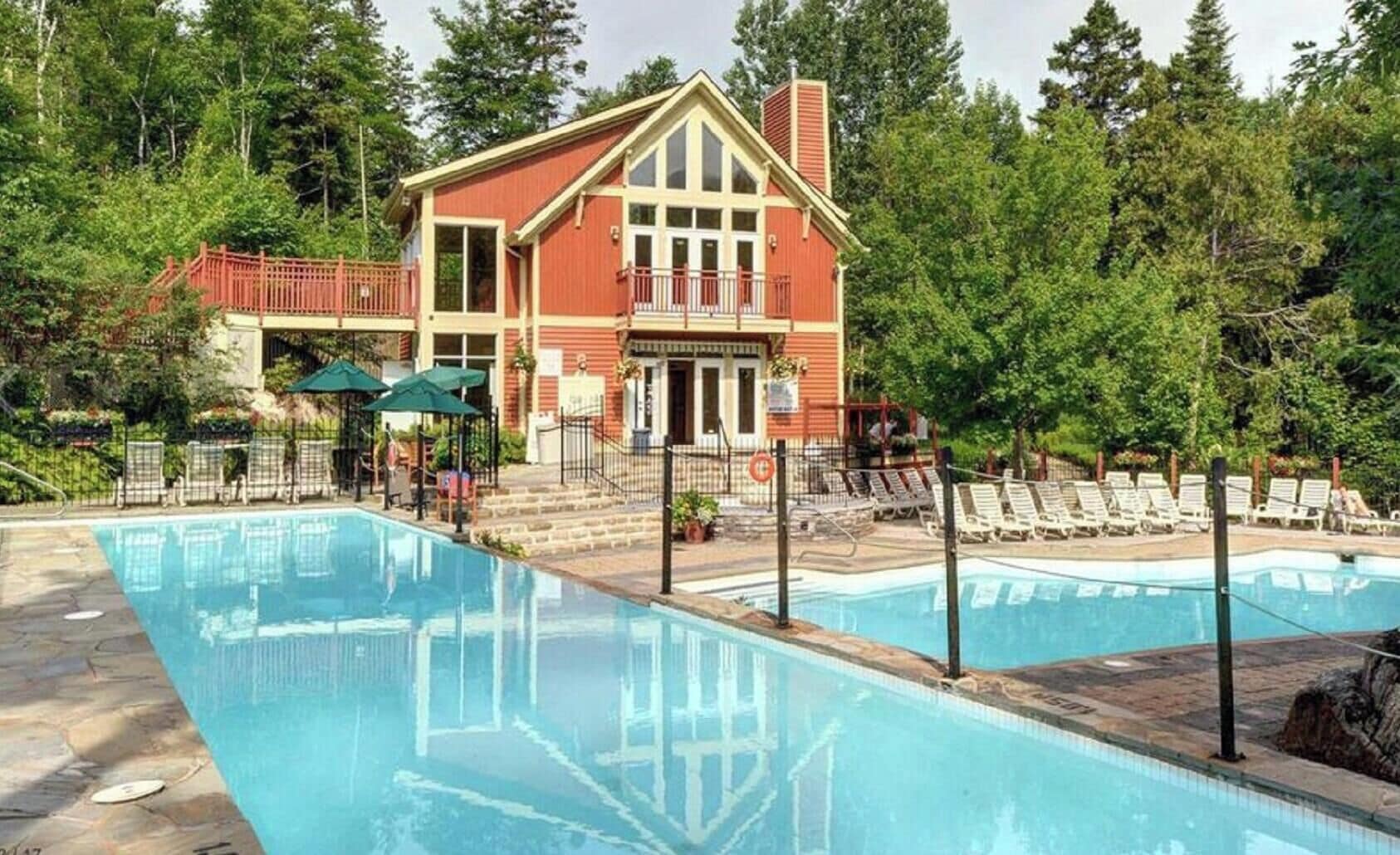 A poolside view of a building with a red exterior, a balcony, and a clear blue pool.