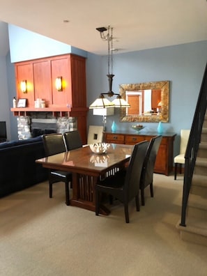 Un comedor con mesa y sillas de madera, chimenea de piedra y una zona de cocina con armarios de madera y encimera azul.