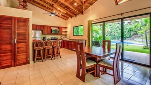 A spacious kitchen with wooden cabinets and a dining area with a large table and chairs. - Hidden Palms Nosara (Nosara)
