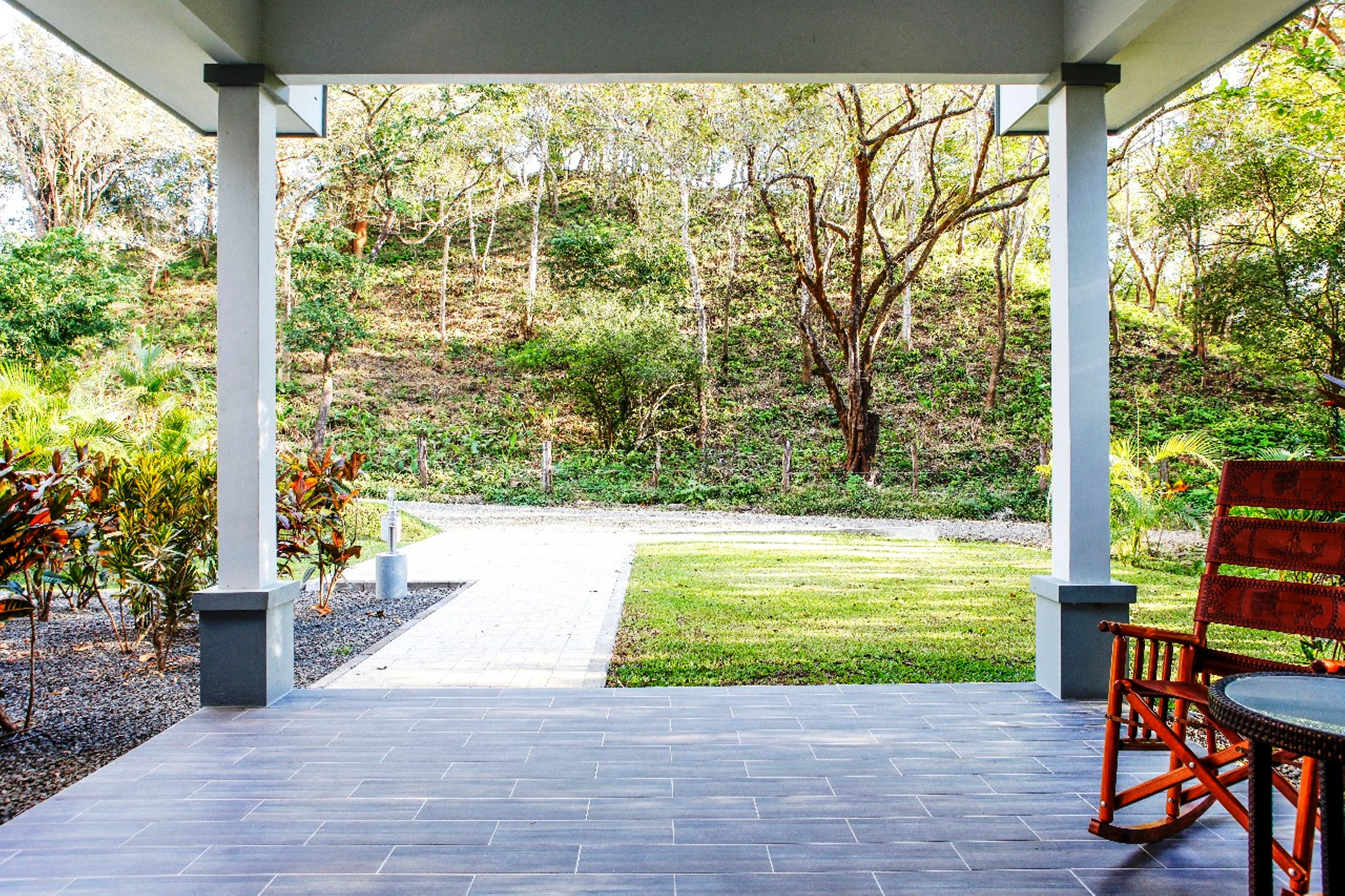 Un patio cubierto con vistas a un jardín ajardinado y un sendero que conduce a una zona verde.