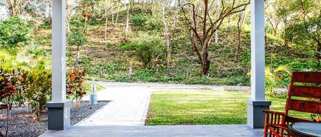 Un patio cubierto con vistas a un jardín ajardinado y un sendero que conduce a una zona verde.