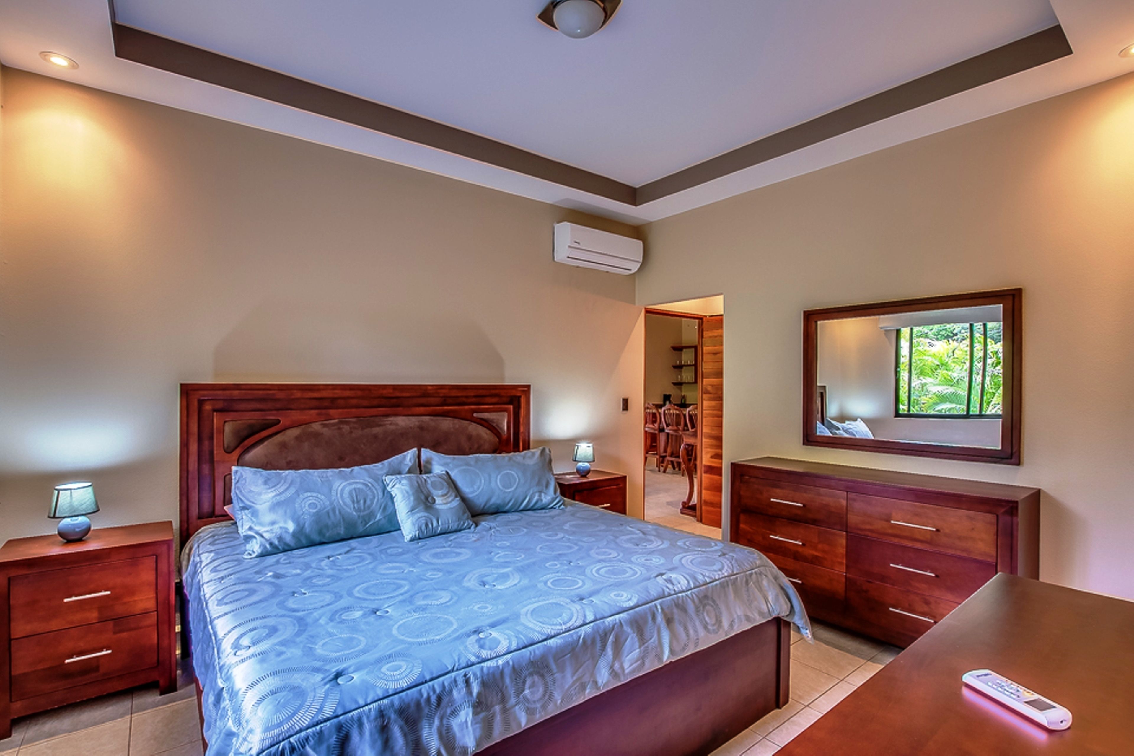 A bedroom with a large bed, wooden headboard, bedside tables, a dresser, and a mirror on the wall.