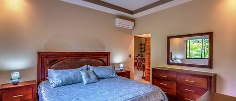 A bedroom with a large bed, wooden headboard, bedside tables, a dresser, and a mirror on the wall.
