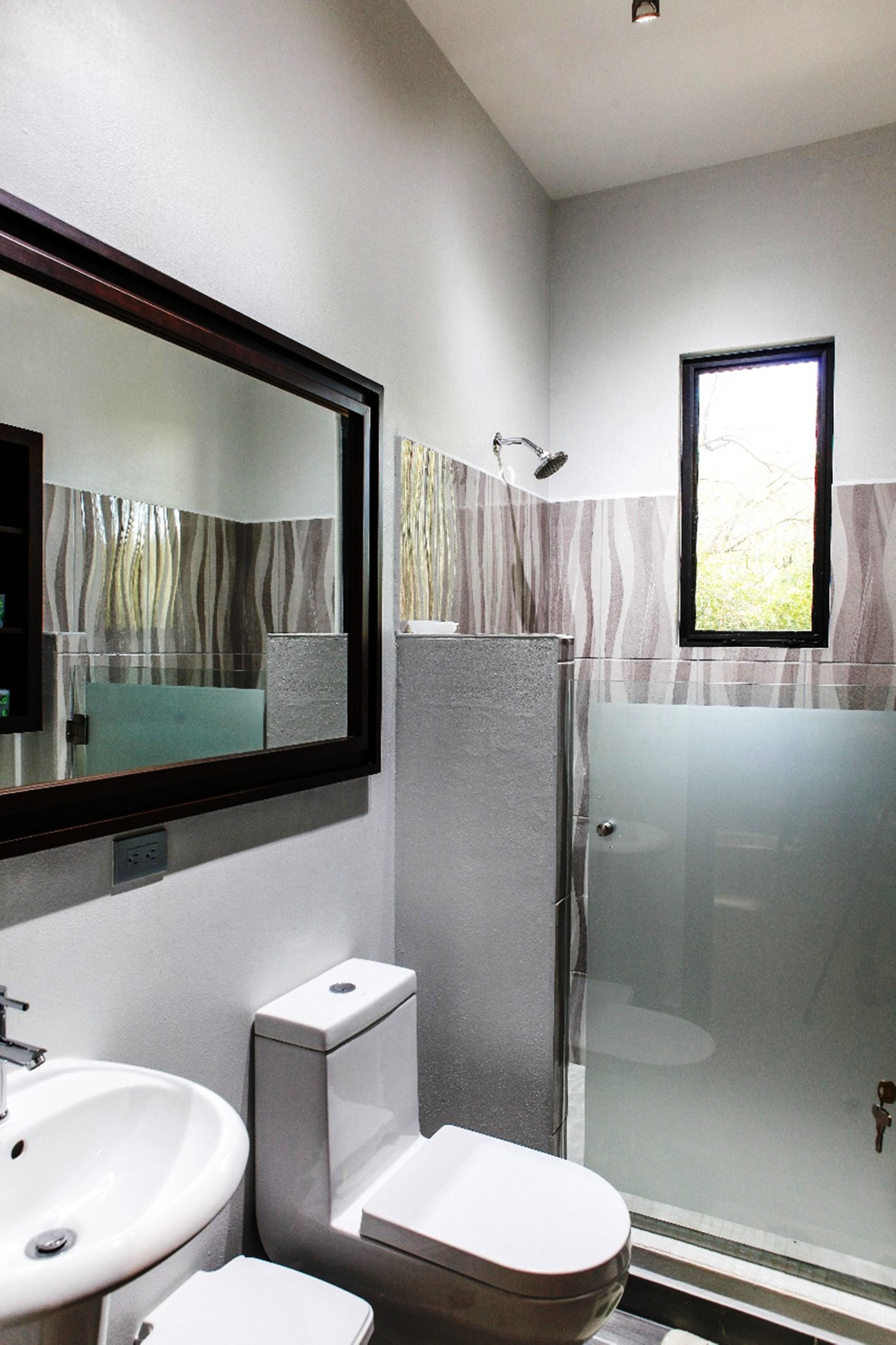 A modern bathroom with a large mirror, two sinks, a toilet, and a glass-enclosed shower.