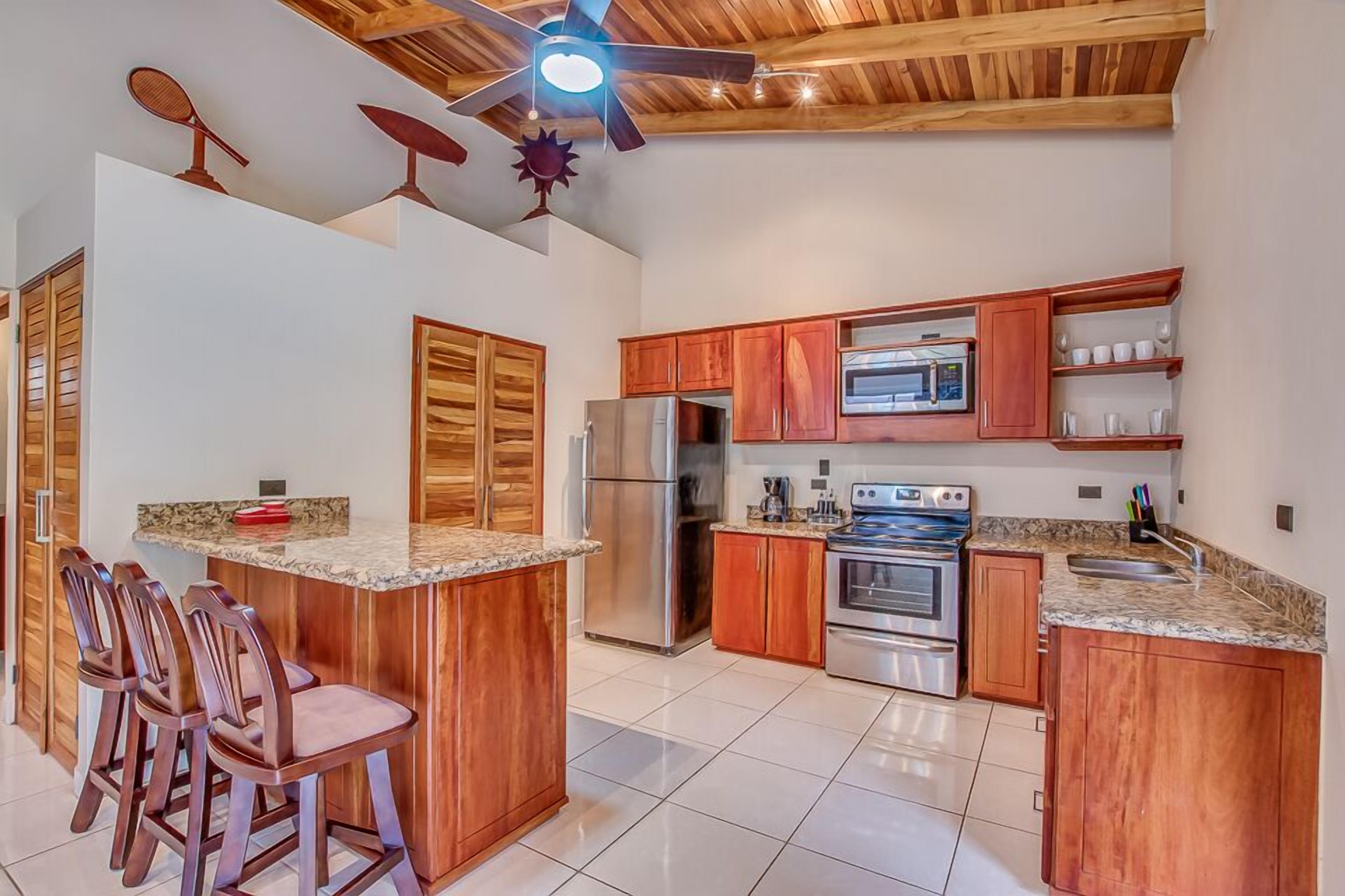 Une cuisine avec des meubles en bois, un îlot central doté de tabourets, des appareils électroménagers en acier inoxydable et un ventilateur de plafond.