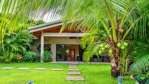 A modern house with a covered porch, a stone pathway leading to the entrance, and lush tropical vegetation. - Hidden Palms Nosara (Nosara)