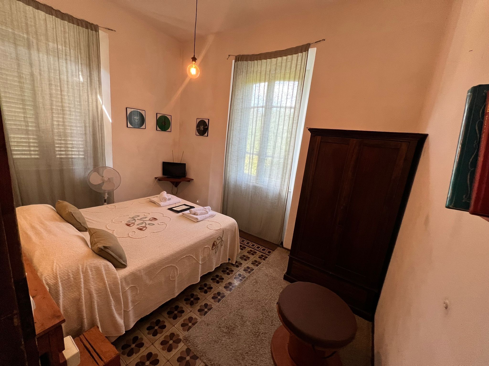 Une chambre à coucher comprenant un lit, un bureau, une chaise, un ventilateur et une armoire.