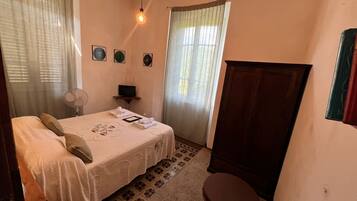 Une chambre à coucher comprenant un lit, un bureau, une chaise, un ventilateur et une armoire.
