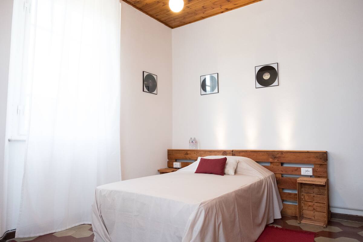 Un dormitorio con cabecera de madera, cama con ropa de cama blanca y roja, una mesita de noche con lámpara y una pequeña mesa auxiliar de madera.