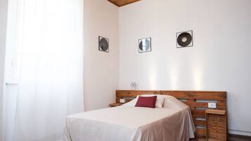 A bedroom with a wooden headboard, a bed with white and red bedding, a nightstand with a lamp, and a small wooden side table.