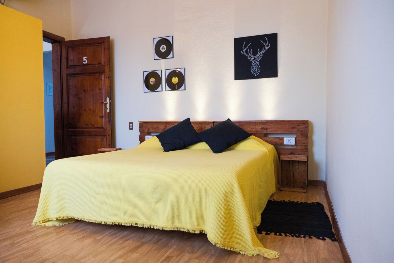 A bedroom with a bed, wooden headboard, a door, and wall decorations including vinyl records and a deer head.