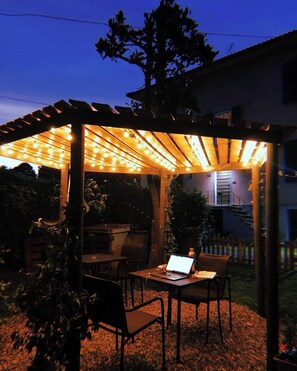 An outdoor patio with a pergola covered in string lights, a laptop on a table, and chairs. - Villa Sunrise (Lucca)