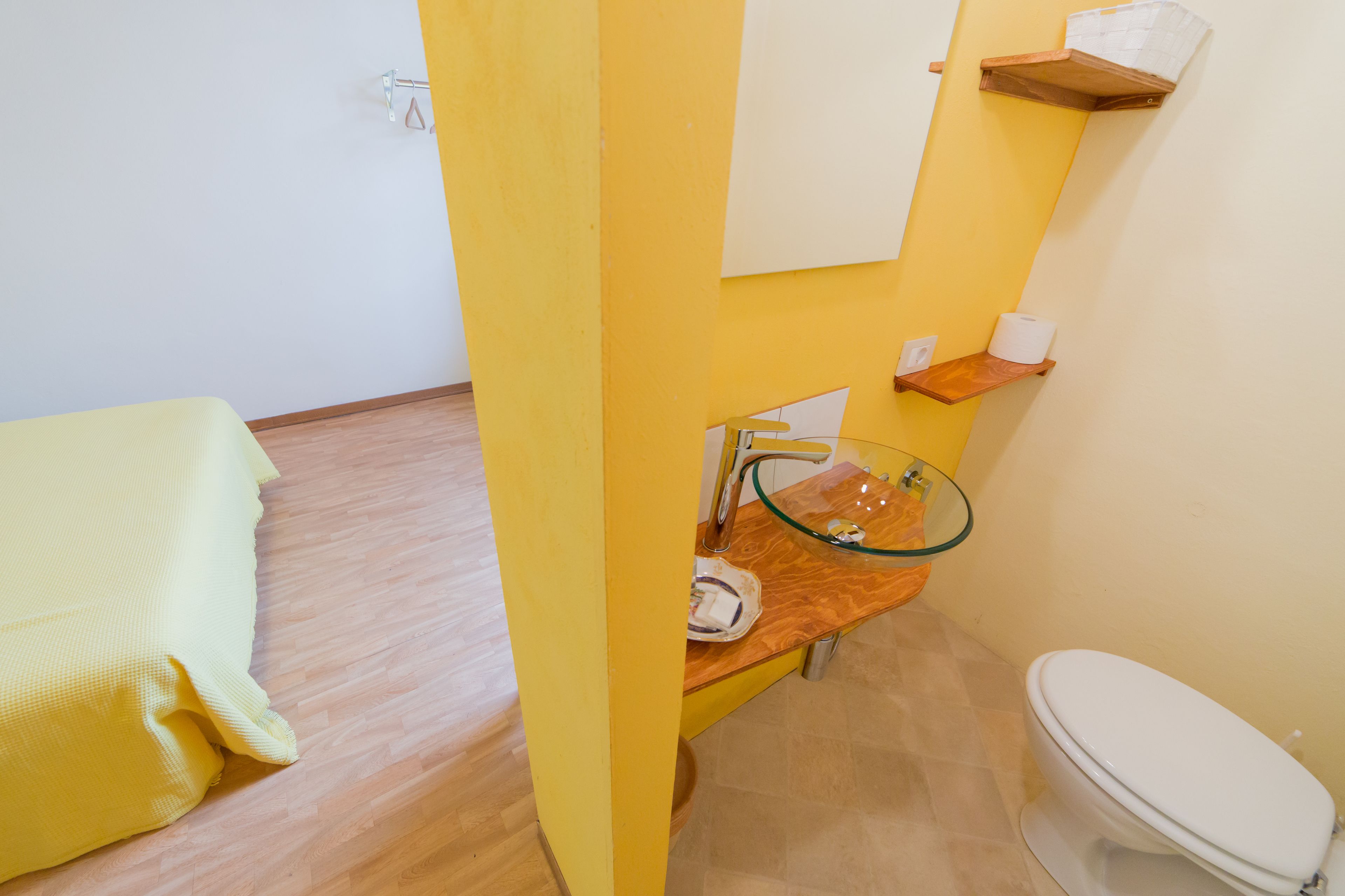 A bathroom with a yellow wall, a wooden countertop, a glass sink, a white toilet, and a towel on the floor.