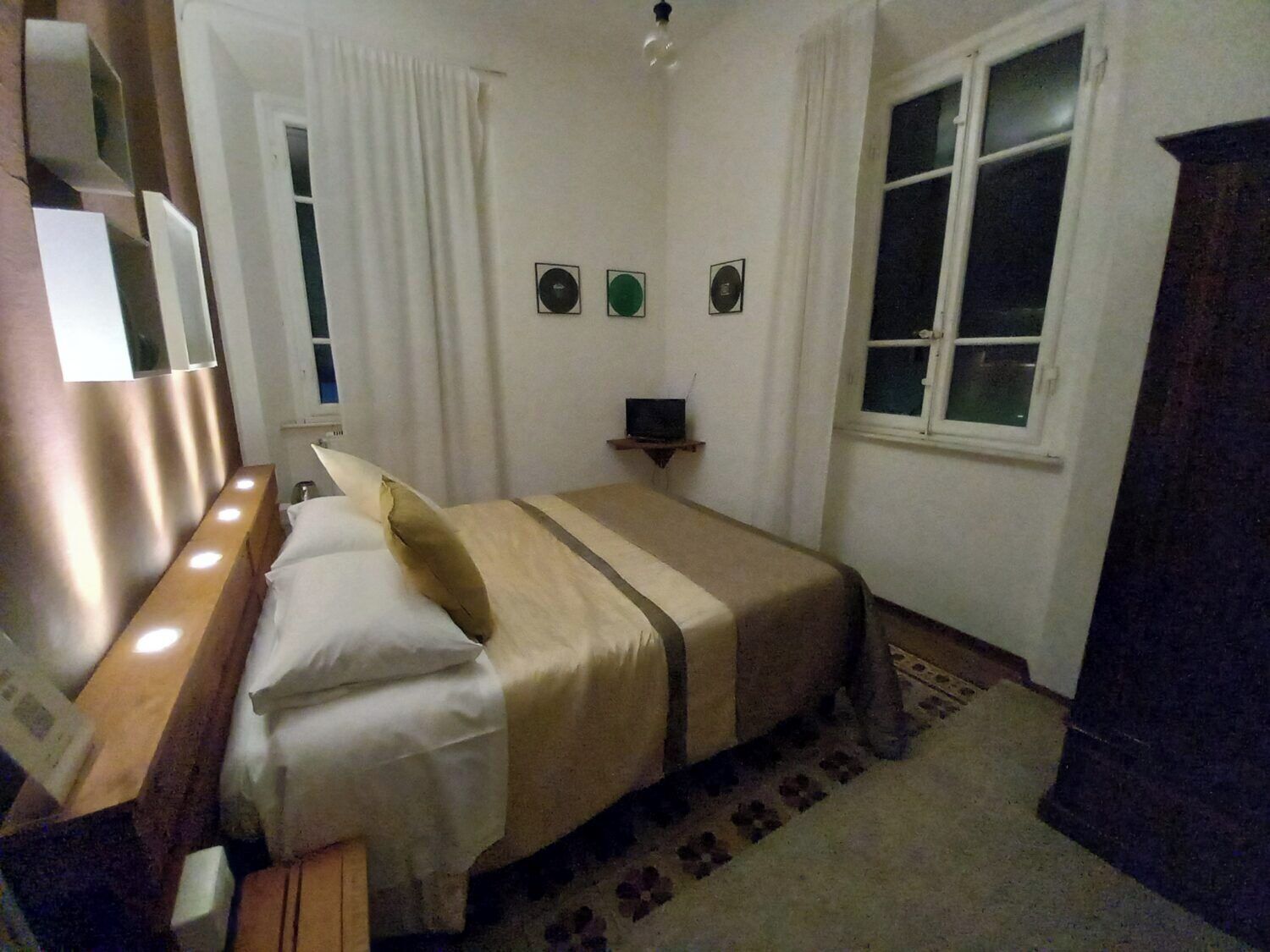 A bedroom with a bed, bedside table, lamp, window, and wall-mounted decorations.