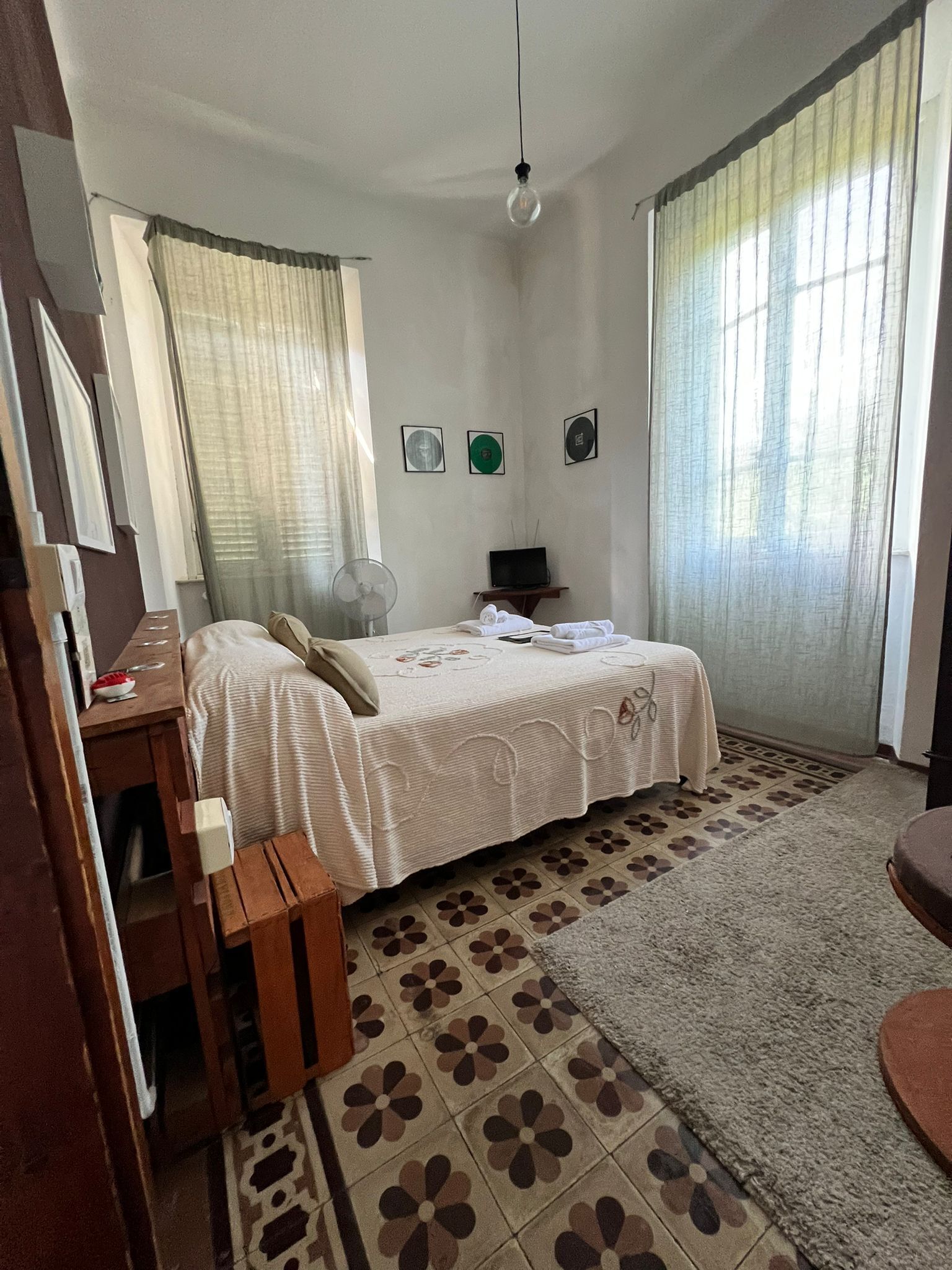 Un dormitorio con cama, escritorio, silla, ventilador y ordenador portátil.