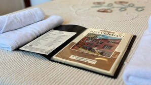Cama bem arrumada com um folheto intitulado "BENENUTO" e um cardápio ao lado.