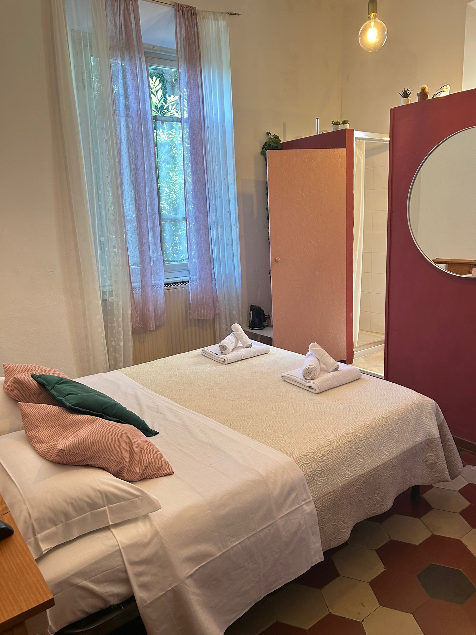A bedroom with two beds, a mirror, a wardrobe, and a window with curtains.