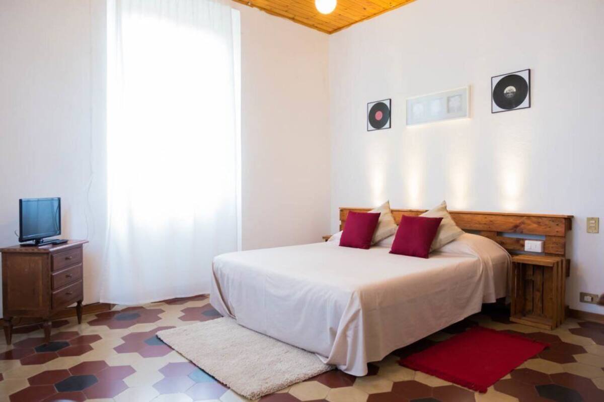Un dormitorio con una cama, un televisor sobre un mueble de madera y una ventana con cortinas.