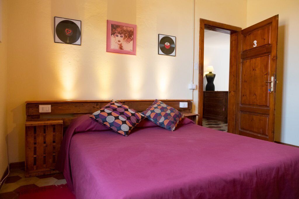 Une chambre avec une tête de lit en bois, une couvre-lit violette et deux coussins à motifs. On peut voir deux disques vinyle et un tableau encadré accrochés au mur.