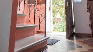 Uma escadaria com grades de metal decoradas leva a um segundo andar. Uma porta de madeira e uma janela são visíveis no patamar.