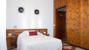 A bedroom with a wooden headboard, two framed vinyl records on the wall, a bed with white bedding and a red pillow, a wooden wardrobe, and a door labeled "2".