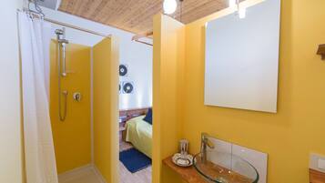 Une salle de bain avec un lavabo en verre, une douche et un lit en arrière-plan.