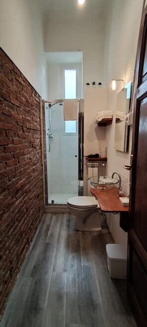A narrow bathroom with a glass shower, a wooden vanity, and a brick wall. - Villa Sunrise (Lucca)