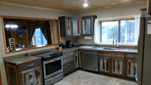 Una cocina con armarios de madera, estufa, lavavajillas y ventana con vistas a árboles.