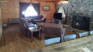 Interior acogedor de una cabaña con paredes de madera, una chimenea de piedra, un sofá, un televisor y una mesa de comedor.