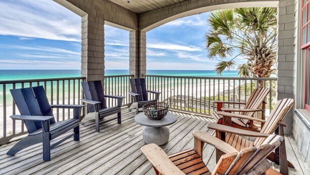 Een houten terras met Adirondack-stoelen en een tafel, met uitzicht op een strand en de oceaan.